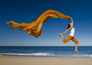 Woman with orange scarf jumping in the beach